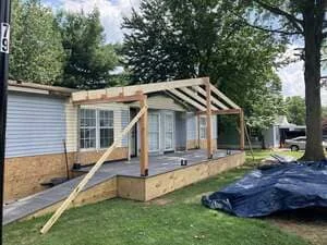 Wood pergola with angled beams attached to front of brick and siding home