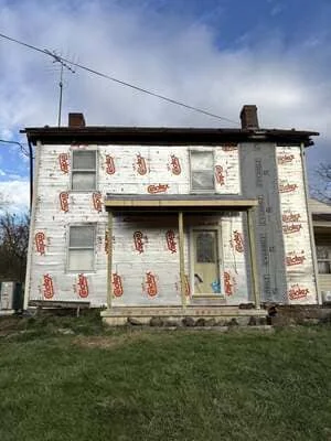 Two-story historic home with white house wrap and red brick chimney during exterior renovation
