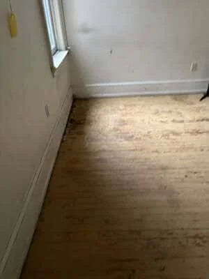 Interior room with prepared wooden subfloor, white drywall walls, and baseboard trim installation