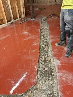 Red epoxy-sealed concrete basement floor with control joint and drainage channel