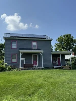 Gray-blue sided house with new roof, solar panels, and front porch addition on manicured lawn